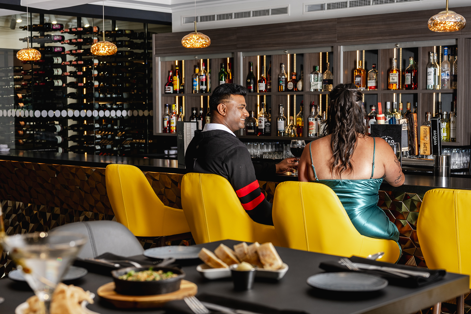 A man and woman sitting at a well stocked bar